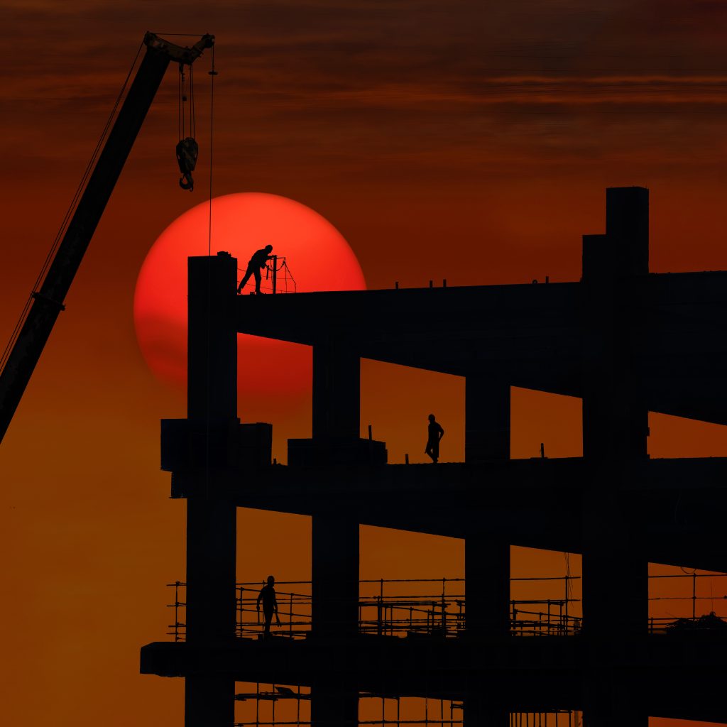 Silhouette of a construction site with workers against a dramatic sunset backdrop.